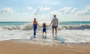 Rodzina trzymająca się za ręce na plaży, fale rozbijające się o brzeg.