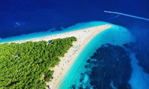Widok z lotu ptaka na plażę w kształcie rogu obfitości, otoczoną turkusową wodą i zielonym lasem.