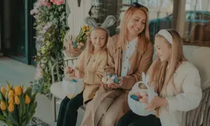 Rodzina z koszykami wielkanocnymi i pisankami siedzi na zewnątrz, otoczona wiosennymi dekoracjami.
