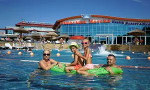 Rodzina pływa w basenie przy hotelu "Panorama Morska" z widokiem na budynek.