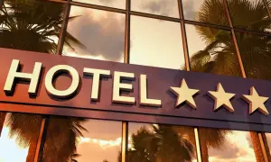 Napis "HOTEL" z trzema gwiazdkami na tle odbijających się palm i nieba.