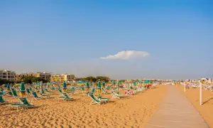 Szeroka, piaszczysta plaża w Bibione z rzędami leżaków i parasoli pod błękitnym niebem.