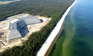 Nowy hotel w kształcie litery V nad Bałtykiem, otoczony lasem i plażą.