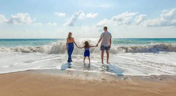 Rodzina trzymająca się za ręce na plaży, fale rozbijające się o brzeg.