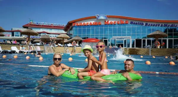 Rodzina pływa w basenie przy hotelu "Panorama Morska" z widokiem na budynek.