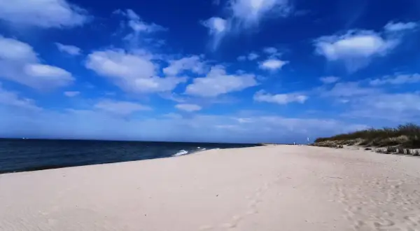 Pusta piaszczysta plaża nad Bałtykiem, błękitne niebo z chmurami, morze.