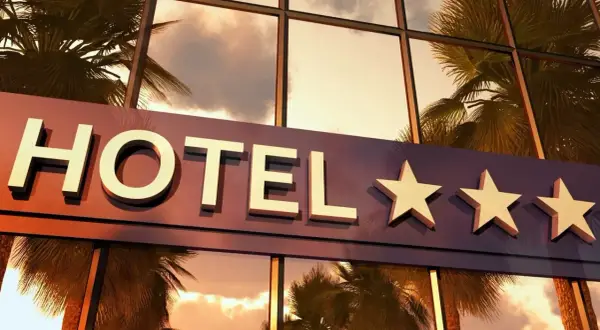 Napis "HOTEL" z trzema gwiazdkami na tle odbijających się palm i nieba.
