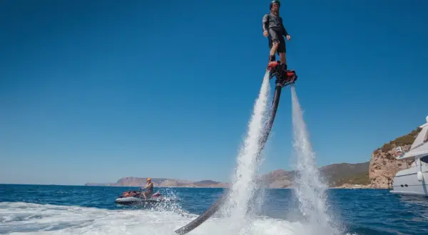 Mężczyzna na flyboardzie i osoba na skuterze wodnym na tle morza i klifów.
