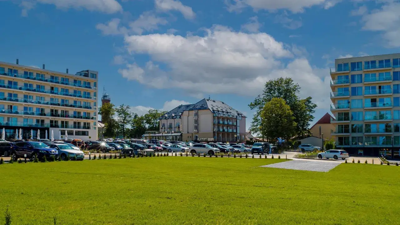 Nowoczesne budynki hotelowe i parking pełen samochodów na tle błękitnego nieba z chmurami.
