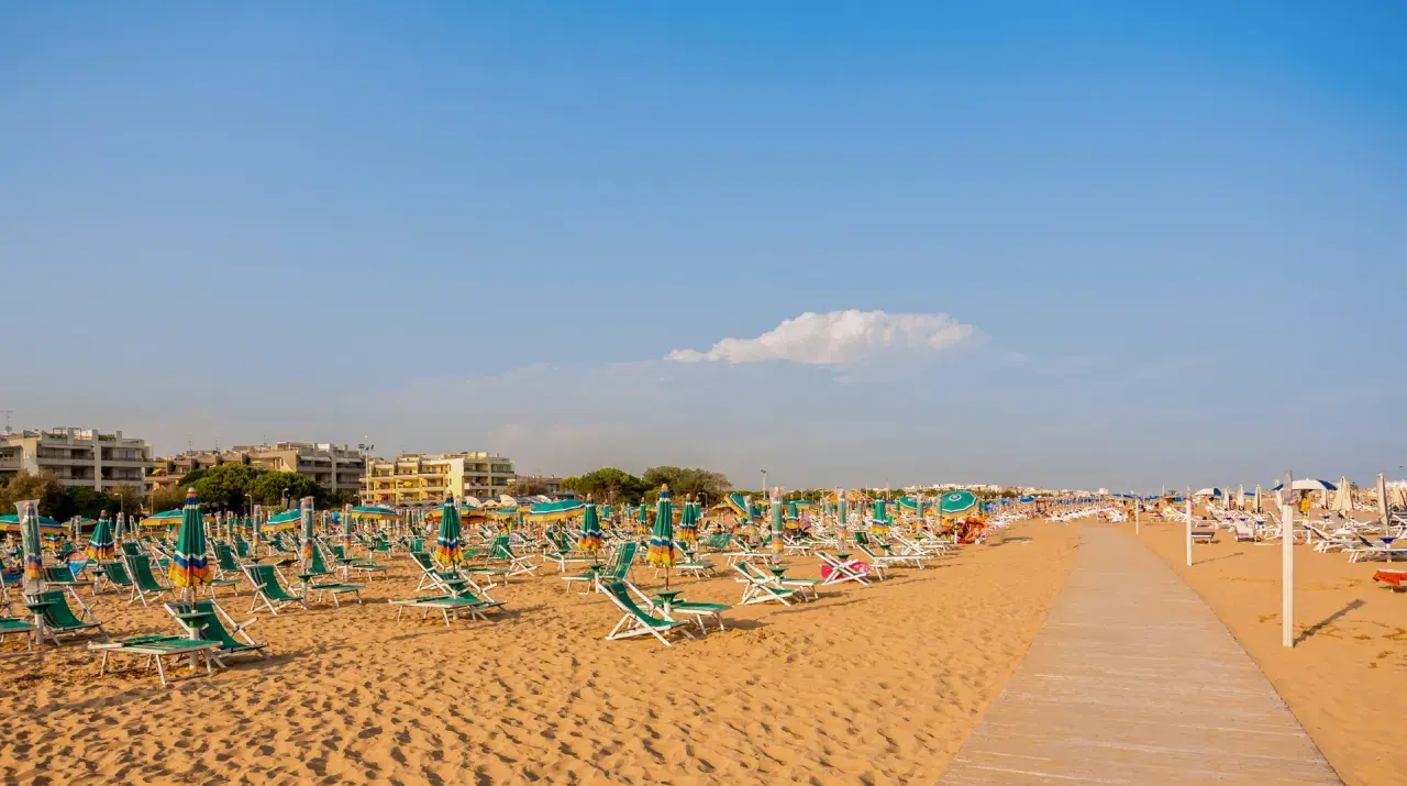 Szeroka, piaszczysta plaża w Bibione z rzędami leżaków i parasoli pod błękitnym niebem.