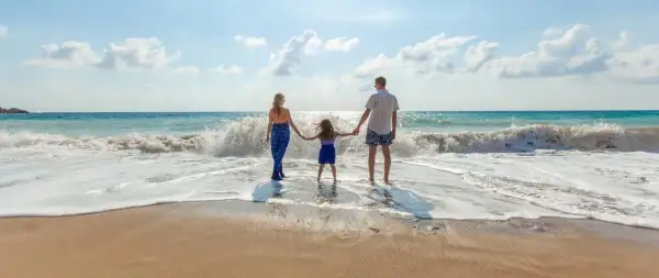 Rodzina trzymająca się za ręce na plaży, fale rozbijające się o brzeg.