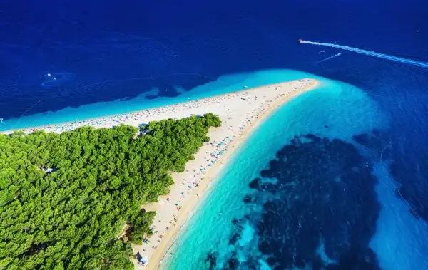 Widok z lotu ptaka na plażę w kształcie rogu obfitości, otoczoną turkusową wodą i zielonym lasem.