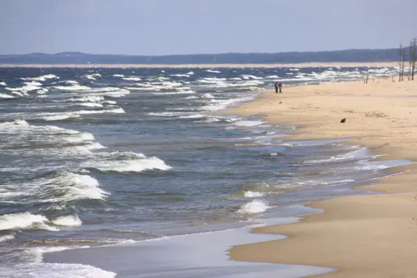 Plaża nad wzburzonym morzem, dwie osoby spacerują brzegiem.