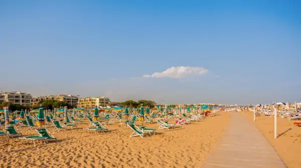 Szeroka, piaszczysta plaża w Bibione z rzędami leżaków i parasoli pod błękitnym niebem.