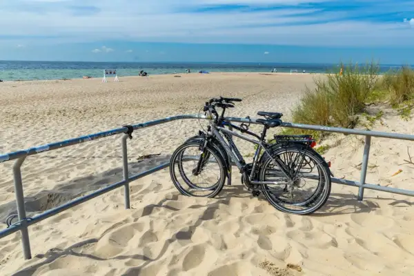 Dwa rowery stojące na piaszczystej plaży, z widokiem na morze i błękitne niebo.