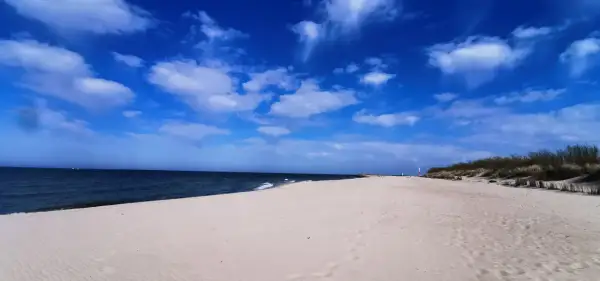 Pusta piaszczysta plaża nad Bałtykiem, błękitne niebo z chmurami, morze i wydmy.