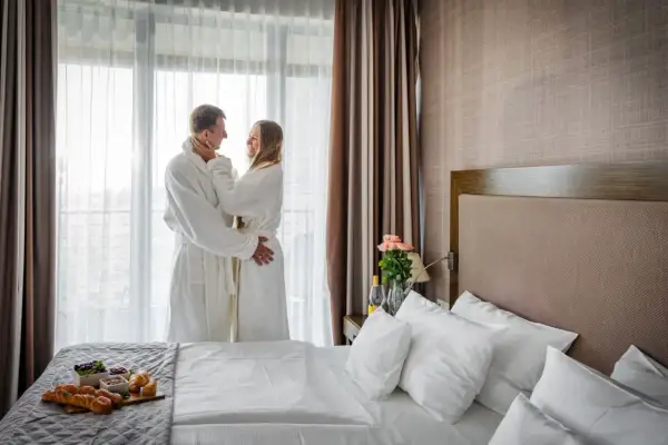 Para w szlafrokach przy oknie, romantyczny pokój hotelowy z łóżkiem i śniadaniem.