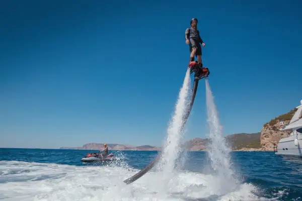 Mężczyzna na flyboardzie i osoba na skuterze wodnym na tle morza i klifów.