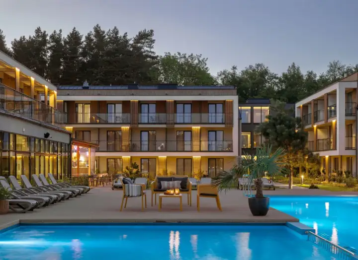 Nowoczesny hotel z basenem i leżakami, otoczony drzewami.